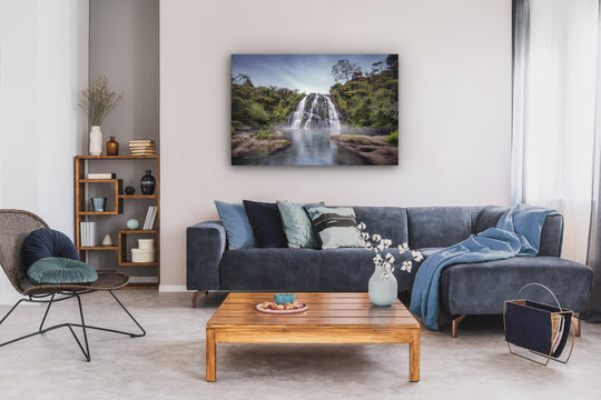 Waterfall photographic print on a wall above a couch, coffee table and chair, in front of a bookcase.