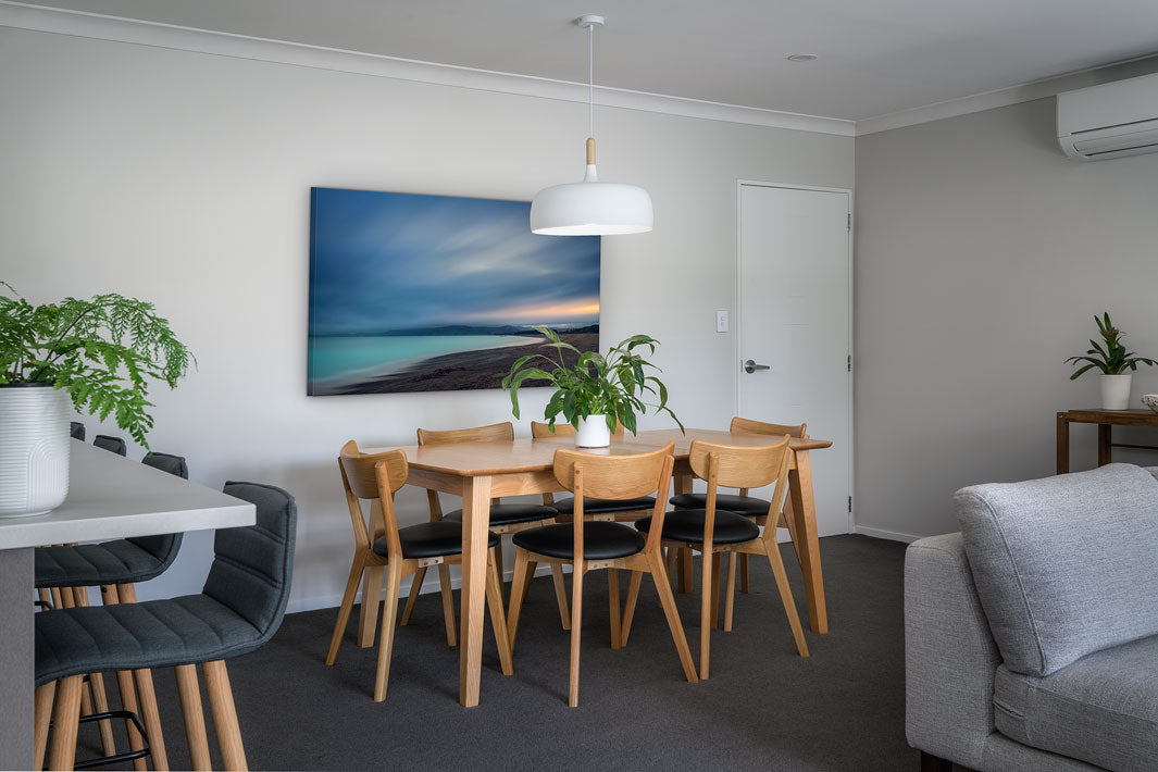 New Zealand landscape on canvas on a wall in a dining room with dining table & chairs, couch & plants