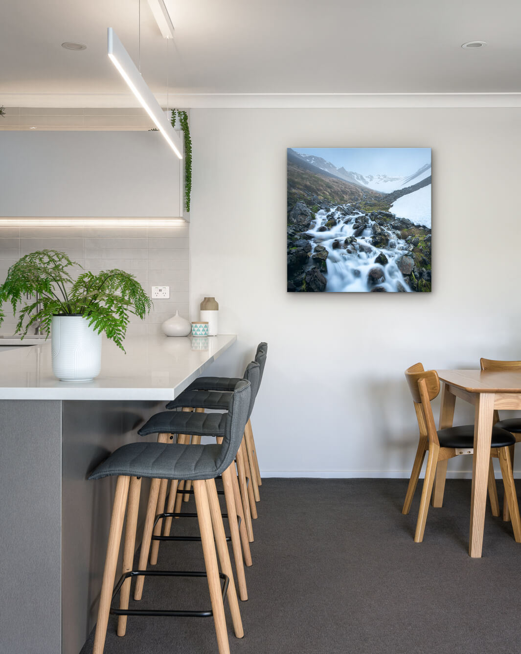 New Zealand landscape photo on canvas in modern kitchen with white bench, barstools, fern and dining setting