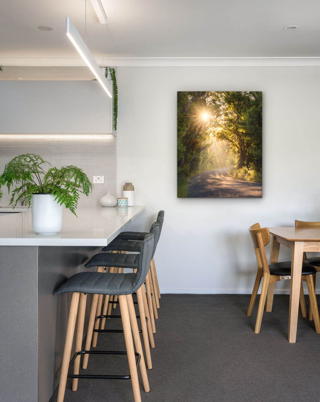 New Zealand landscape photo on canvas in modern kitchen with white bench, barstools, fern and dining setting