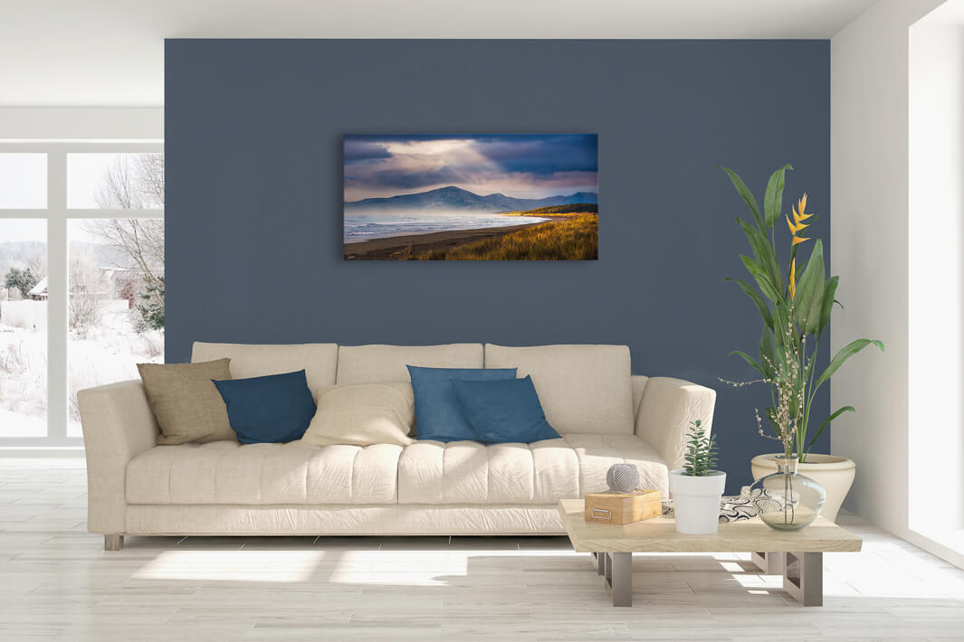 Canvas photo wall art of New Zealand landscape image in lounge setting with a blue wall, white couch, coffee table, plant, cushions