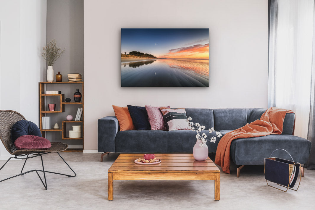 Couch with cushions and throws, coffee table, chair, bookcase and landscape photograph on canvas on the wall above the couch.