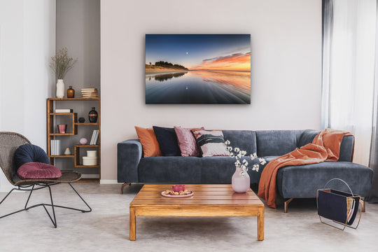 Couch with cushions and throws, coffee table, chair, bookcase and landscape photograph on canvas on the wall above the couch.