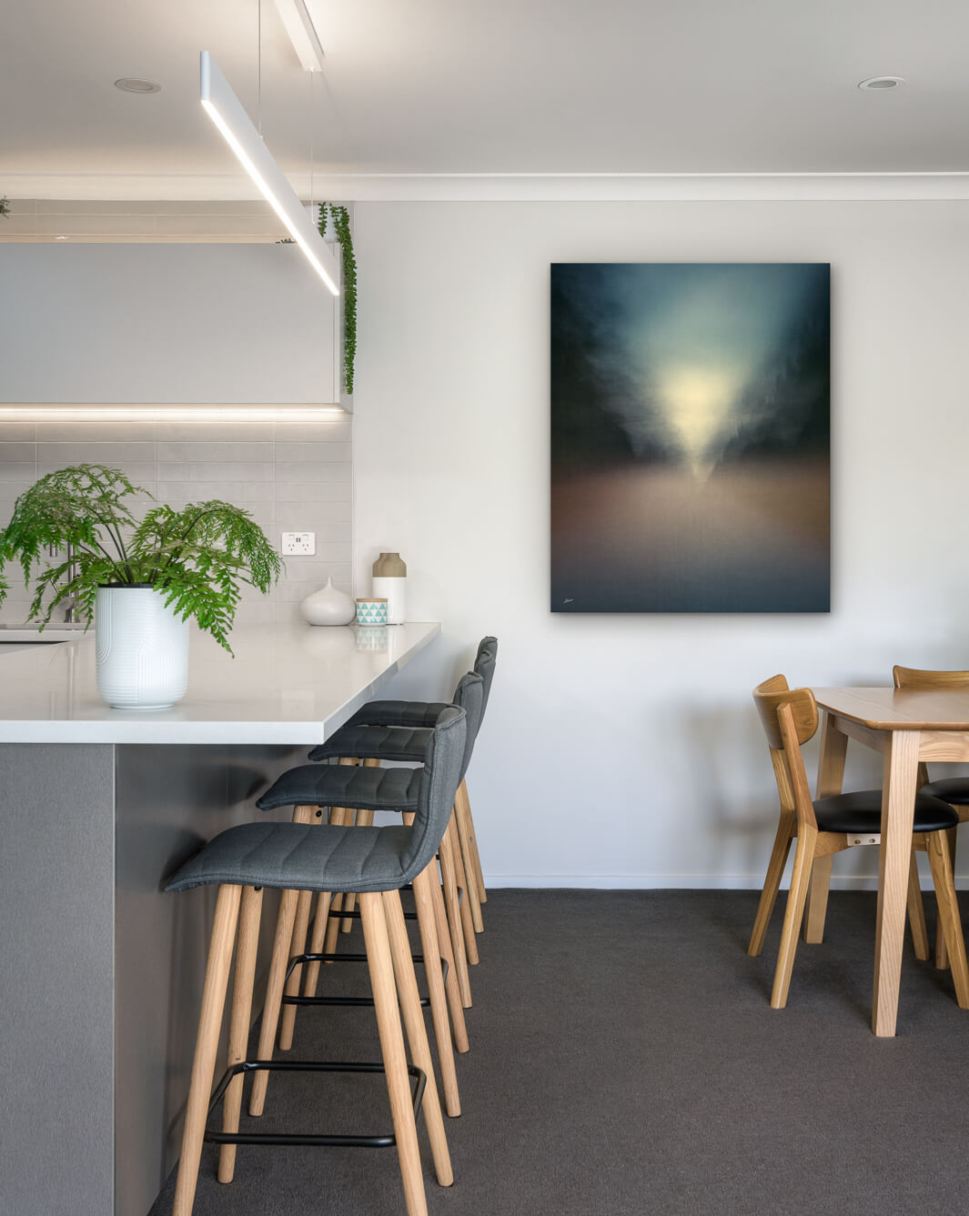 New Zealand landscape photo on canvas in modern kitchen with white bench, barstools, fern and dining setting
