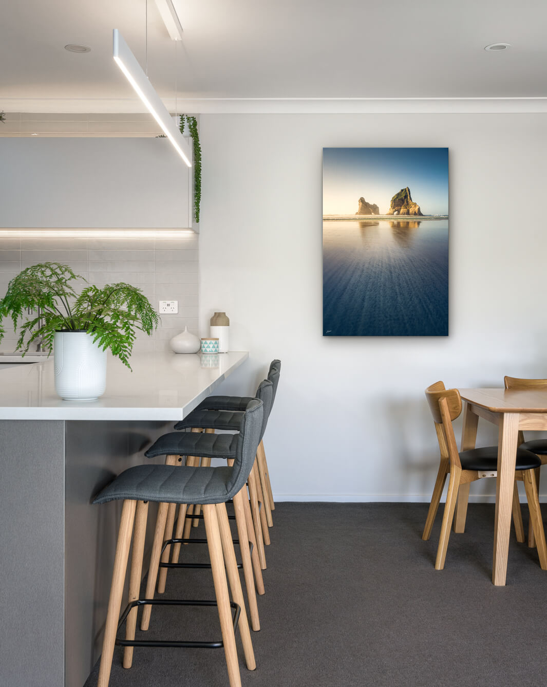 New Zealand landscape photo on canvas in modern kitchen with white bench, barstools, fern and dining setting