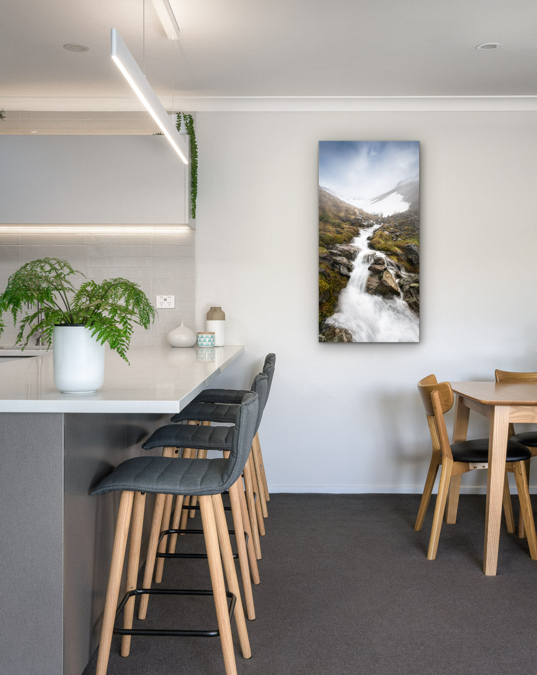 New Zealand landscape photo on canvas in modern kitchen with white bench, barstools, fern and dining setting