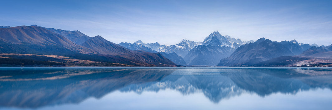 Panoramic landscape photo of Aoraki Mount Cook, New Zealand's highest mountain, reflected in the blue water of Lake Pukaki