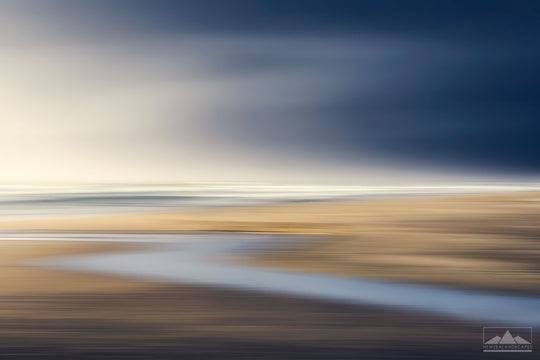 Abstract blurred photo of a stream leading to the beach, with golden sands and dark blue sky