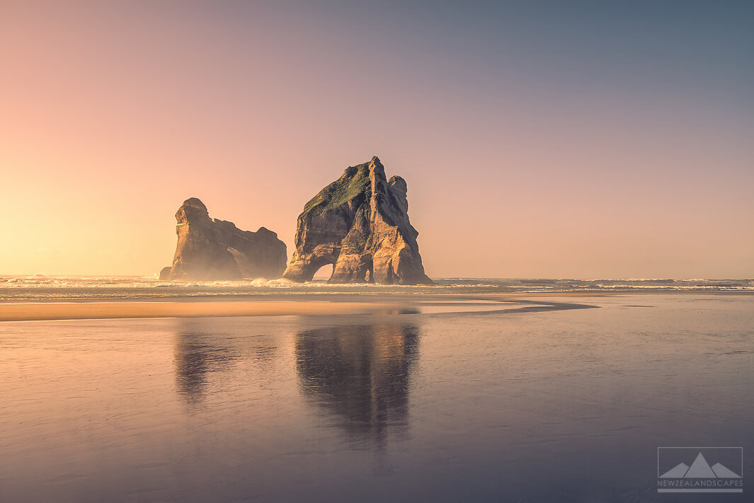 Warm sunset photo of the Archway Island rock stack reflected onto the sand at Wharariki Beach.