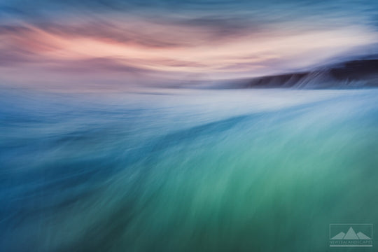 Abstract blurred photo with pink, blue & green hues, of the sea, cliff and sky