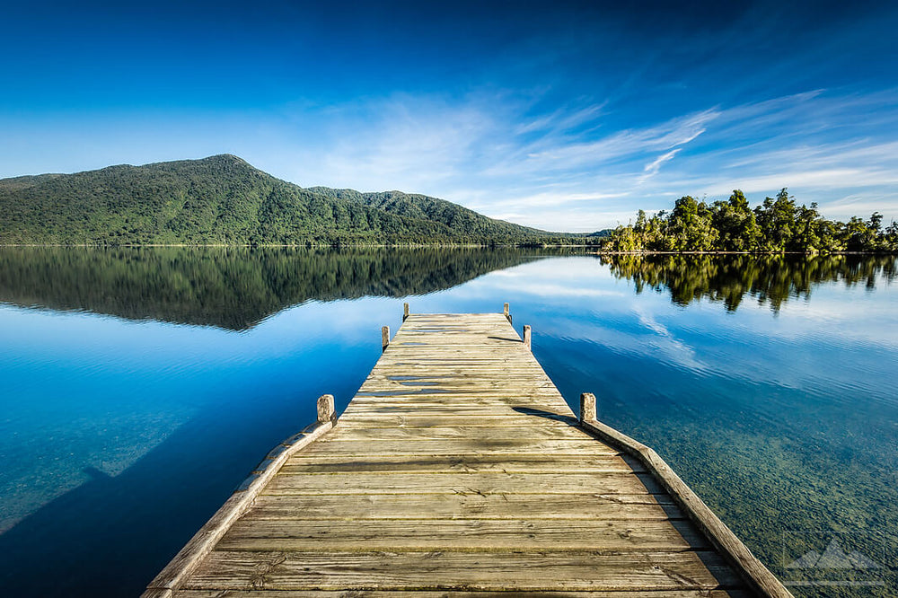 Wooden jetty by blue Lake Kaniere waters with West Coast hills and trees in the foreground