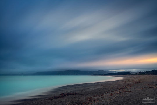 evening photo of a bay with pebbles, smooth long exposure sea and sweeping dramatic clouds.