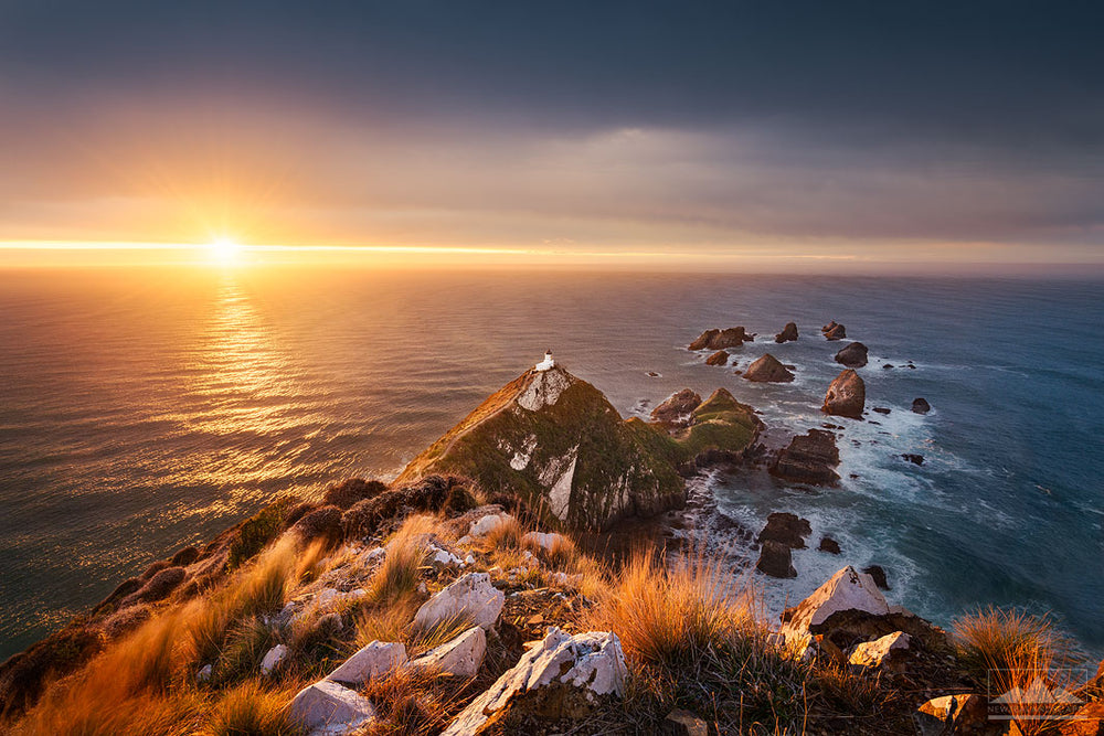 Photo of the sun rising across the ocean at the Nugget Point lighthouse, Otago, New Zealand