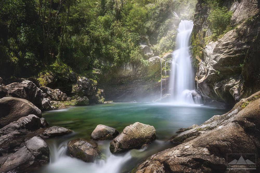 Waterfall into a small water hole below, surrounded by rocks and native New Zealand bush