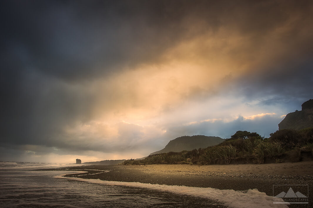 Landscape photo of a storm approaching New Zealand's West Coast with the sea, a rock, trees and mountains in the image