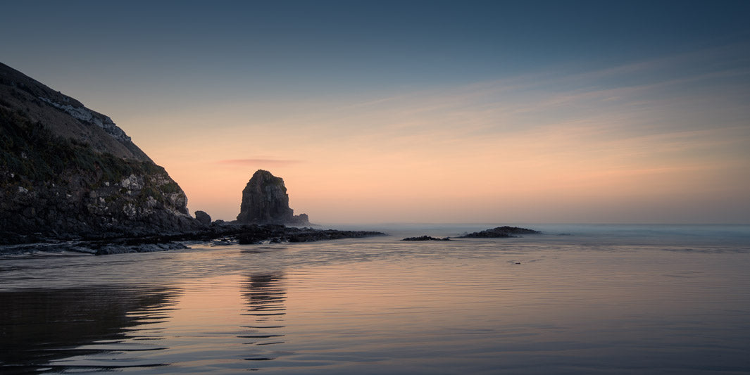 Panorama of a bay at sunset with a monolith reflected in the sea.