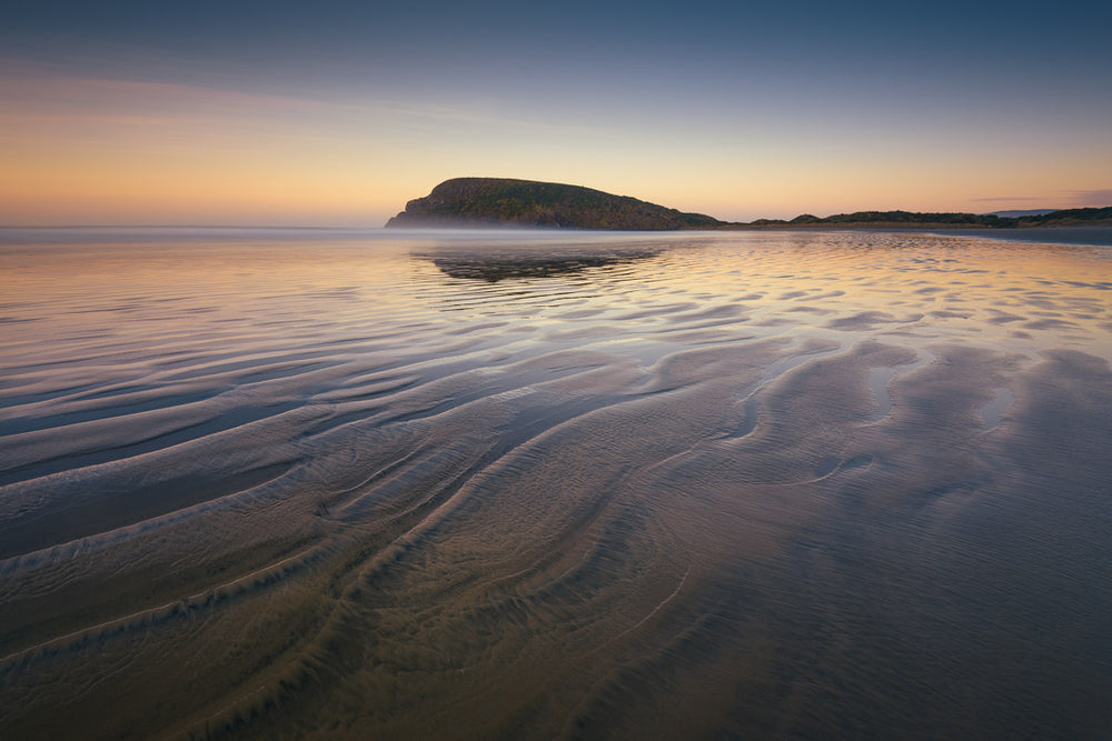 Sunrise behind a hill at Cannibal Bay, with rippling sand and water in the foreground.